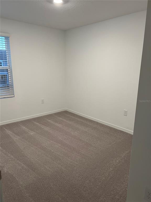 An empty bedroom features white walls, beige carpeting, and a window with blinds — 5080 REVOLUTIONARY WAY, ST CLOUD, FL