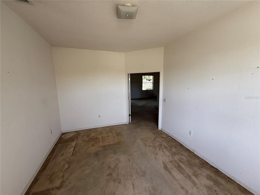 An empty room with beige carpet, white walls, and a doorway leading to another space — 7422 GINGKO AVENUE, LAKELAND, FL