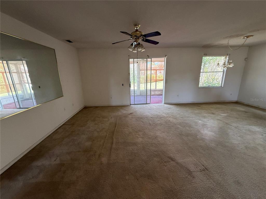 A living room features beige wall-to-wall carpeting, a ceiling fan, and a sliding glass door — 7422 GINGKO AVENUE, LAKELAND, FL
