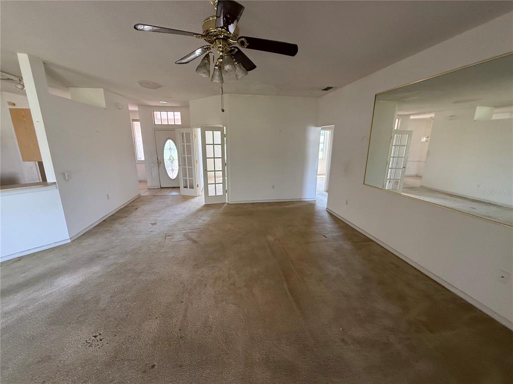 An empty living room features beige carpeting, a ceiling fan, and a large wall mirror — 7422 GINGKO AVENUE, LAKELAND, FL