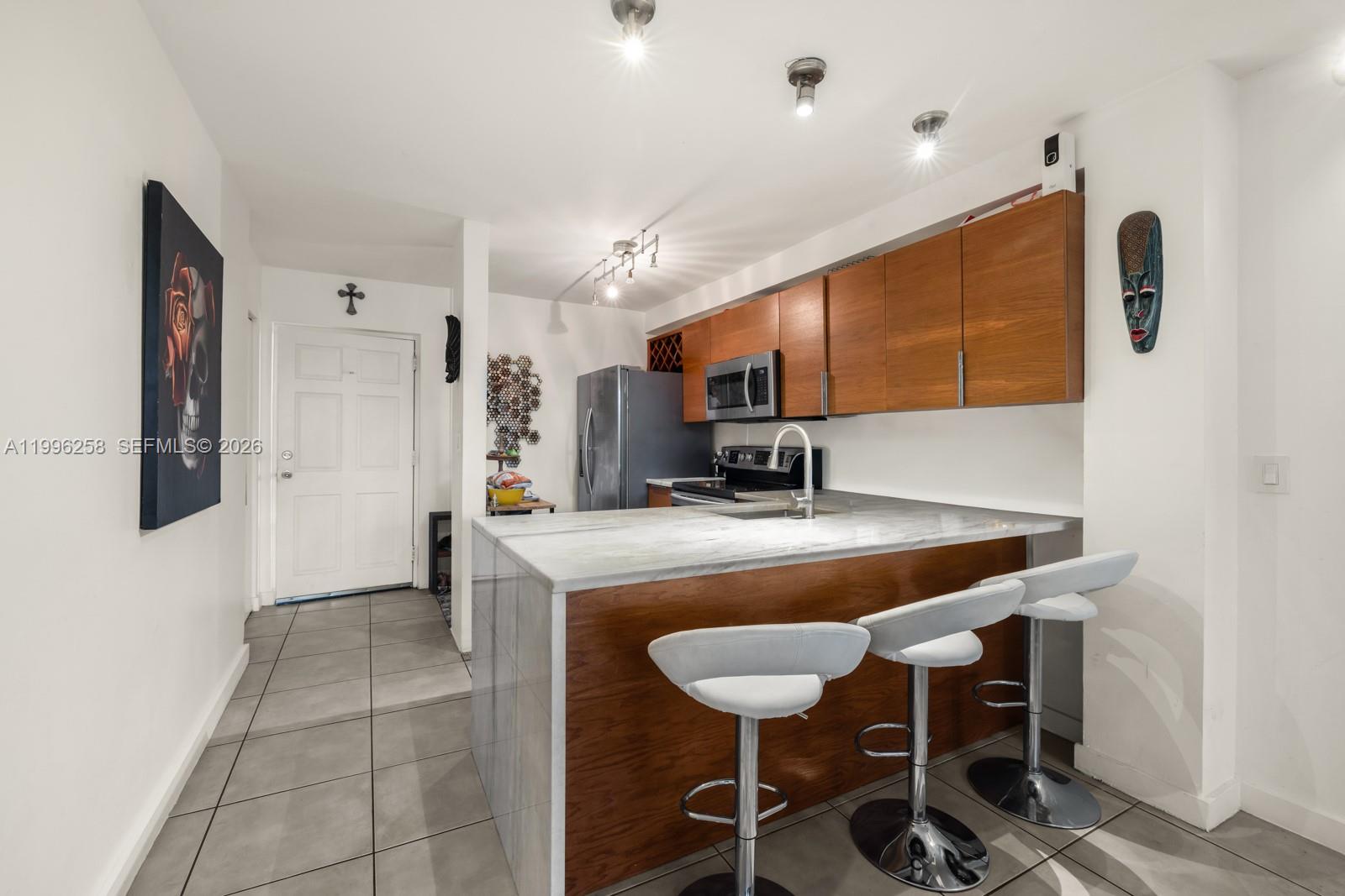 A kitchen features a marble-topped island with white bar stools and wood-toned cabinetry — 680 NE 64th St # A300, Miami FL 33138, MIAMI, FL