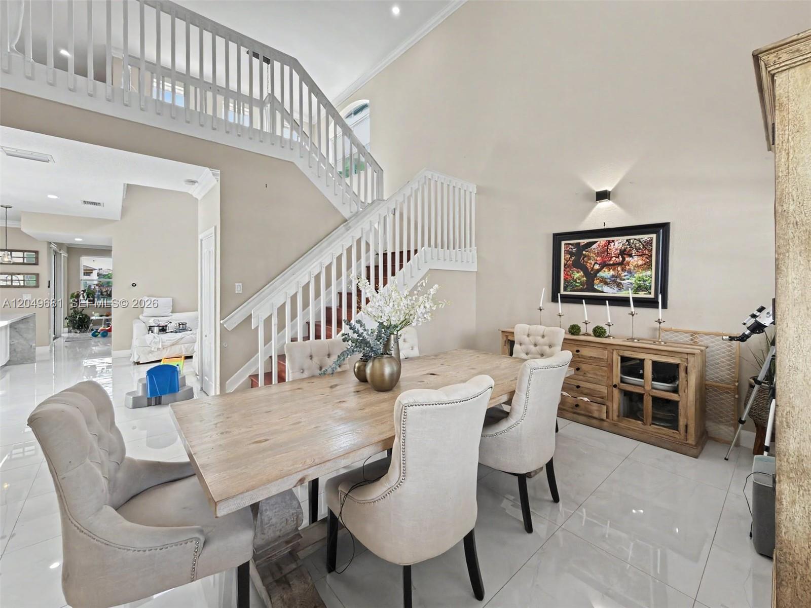 A dining room features a wooden table, upholstered chairs, and a staircase with white railings — 16519 SW 67th Ter, Miami FL 33193, MIAMI, FL