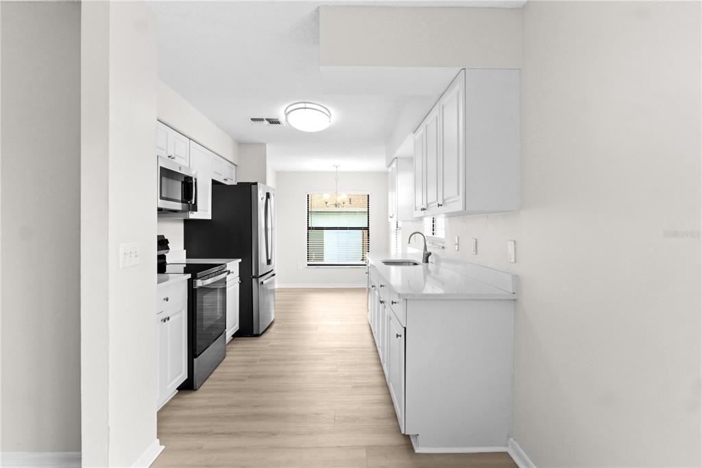 A galley-style kitchen features white cabinets, stainless steel appliances, and light wood-look flooring — 929 SANDYWOOD DRIVE, BRANDON, FL