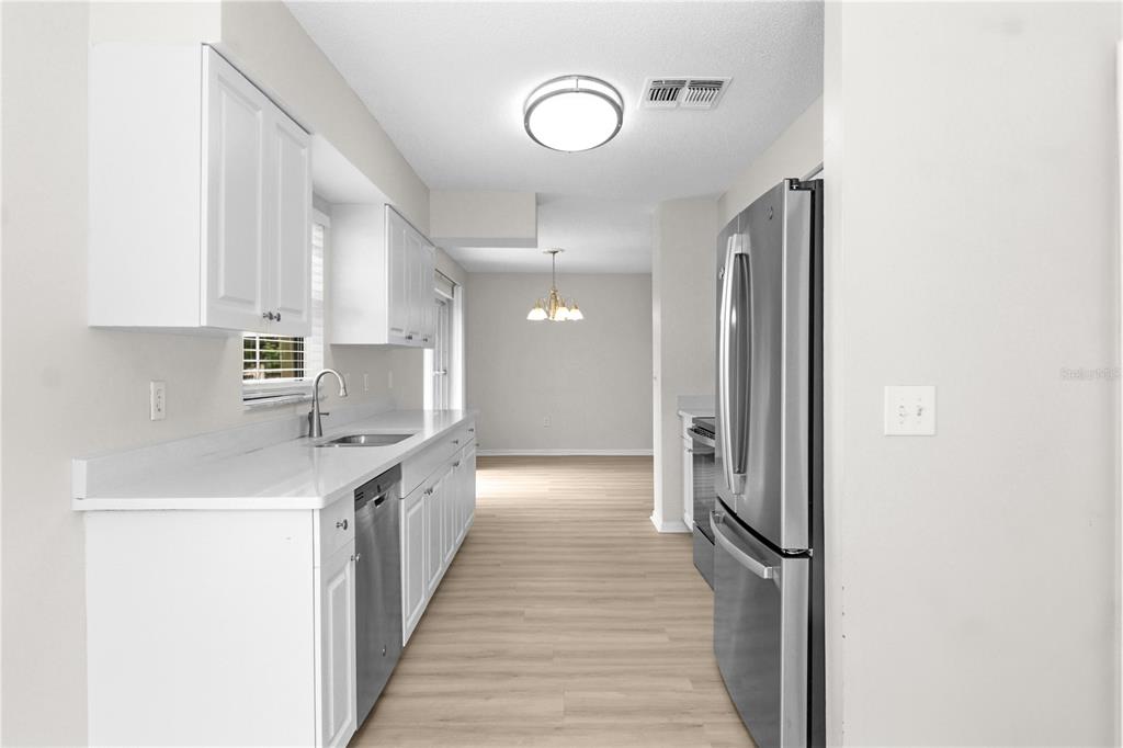 A galley-style kitchen features white cabinets, stainless steel appliances, and light wood-look flooring — 929 SANDYWOOD DRIVE, BRANDON, FL