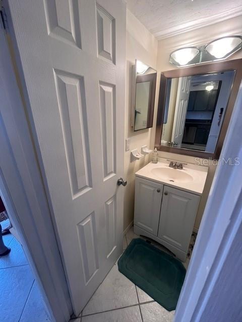 A small bathroom features a white vanity, a wall-mounted mirror, and a tiled floor — 1614 STICKNEY POINT ROAD UNIT 102, SARASOTA, FL