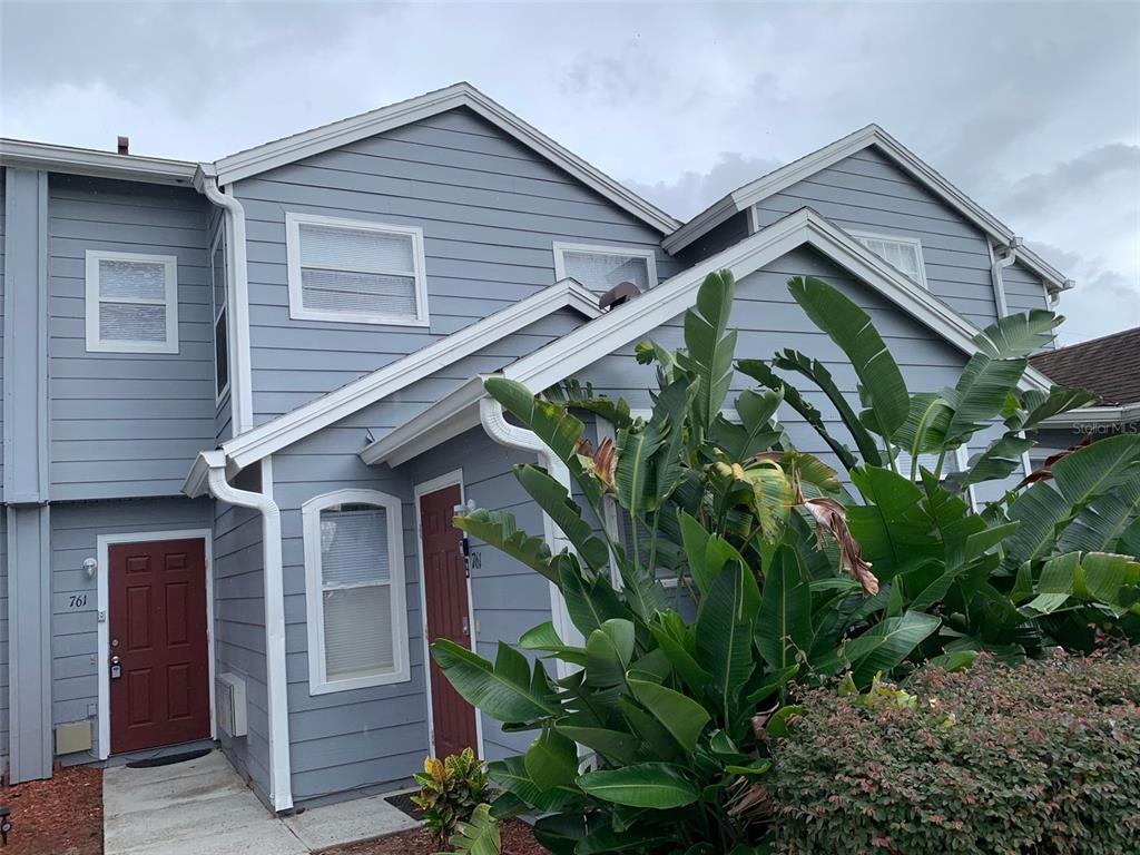 A two-story blue-sided townhouse with a red front door and large tropical plants — 761 CARIBBEAN DRIVE, DAVENPORT, FL