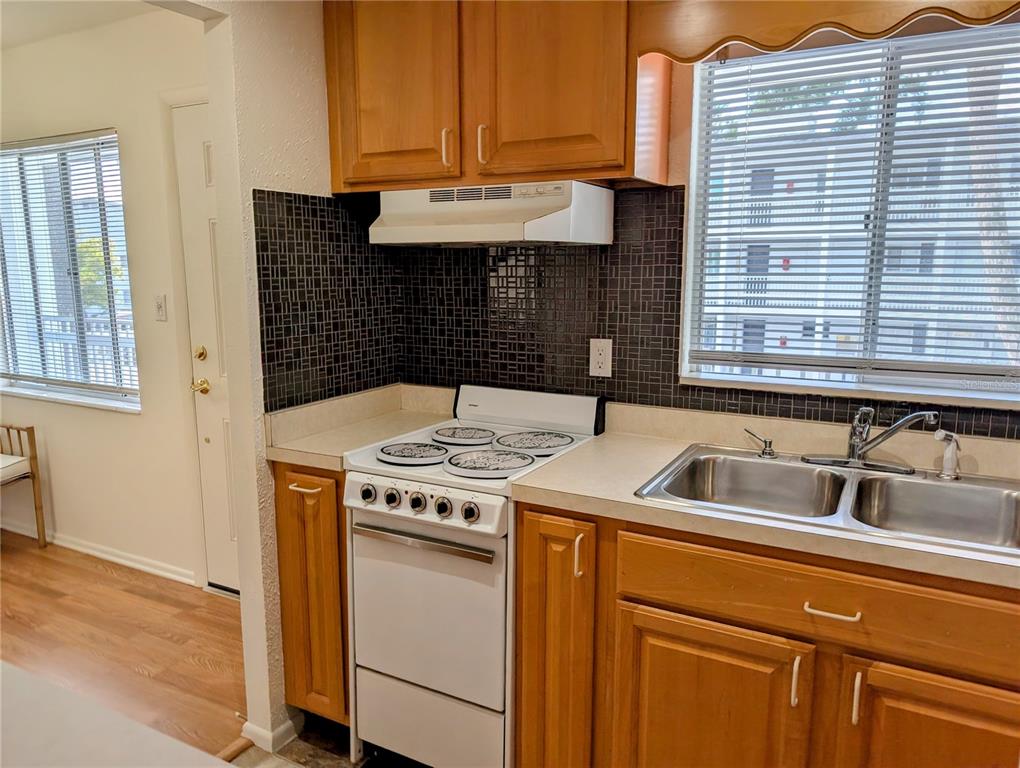 A kitchen features wood cabinets, a white stove, a double sink, and a dark backsplash — 1545 PLEASANT ROAD UNIT H-23, BRADENTON, FL