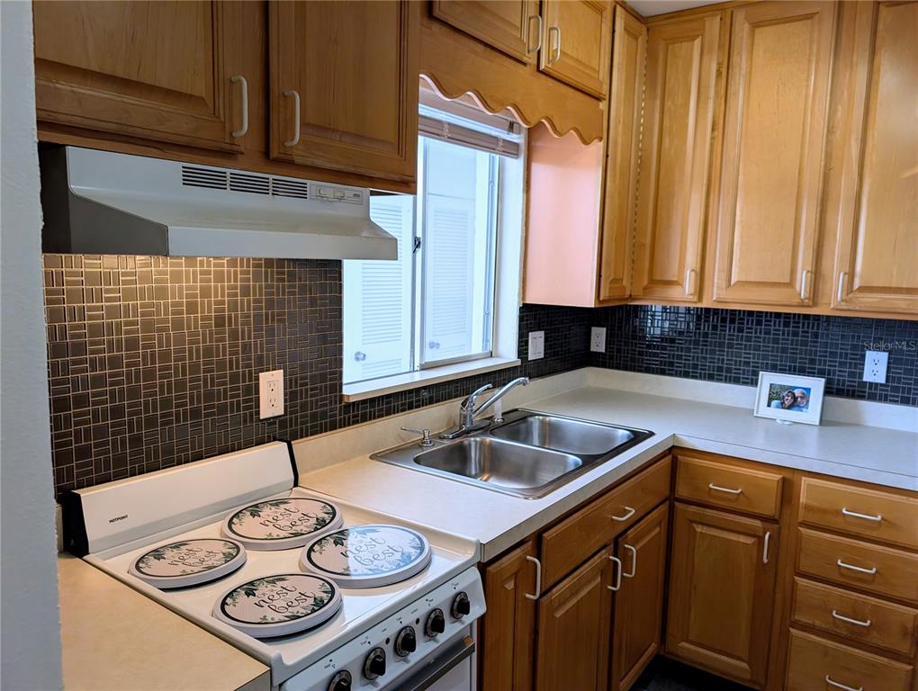 A kitchen features wood cabinets, a white stove with burner covers, and a dark tile backsplash — 1545 PLEASANT ROAD UNIT H-23, BRADENTON, FL
