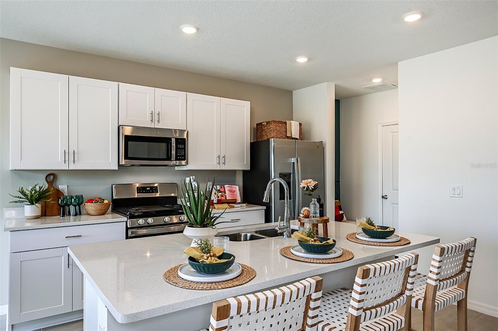 A modern kitchen features white cabinetry, stainless steel appliances, and a large quartz-topped island — 7677 GEMSTONE STREET, GROVELAND, FL