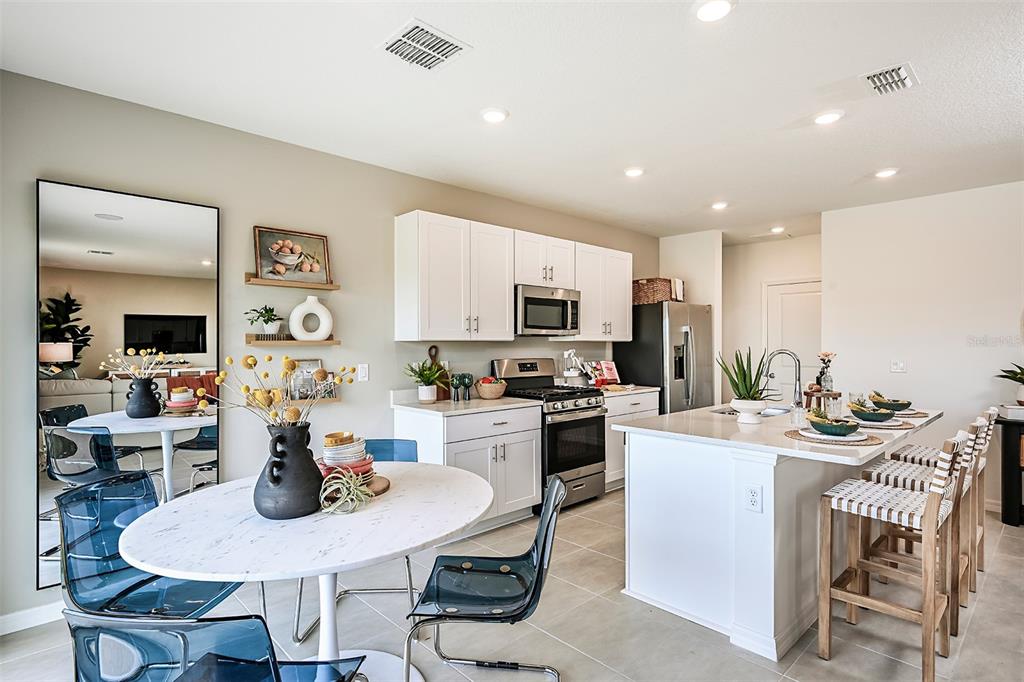 A modern kitchen features white cabinetry, a central island with bar seating, and a dining area — 7677 GEMSTONE STREET, GROVELAND, FL