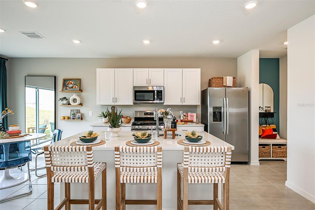 A modern kitchen features white cabinets, stainless steel appliances, and a large central island — 7677 GEMSTONE STREET, GROVELAND, FL