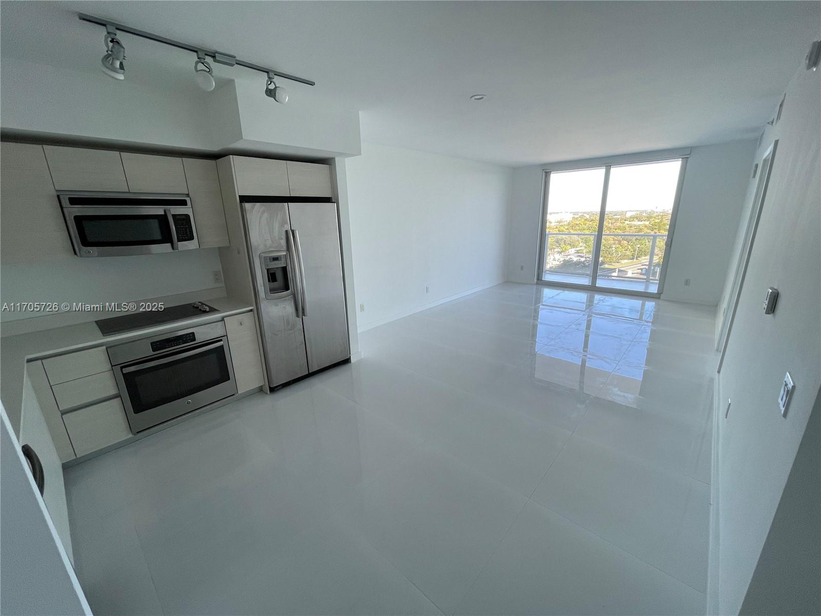 A modern kitchen with stainless steel appliances opens into a bright living area with tile floors — 4250 Biscayne Blvd # 1104, Miami FL 33137, MIAMI, FL