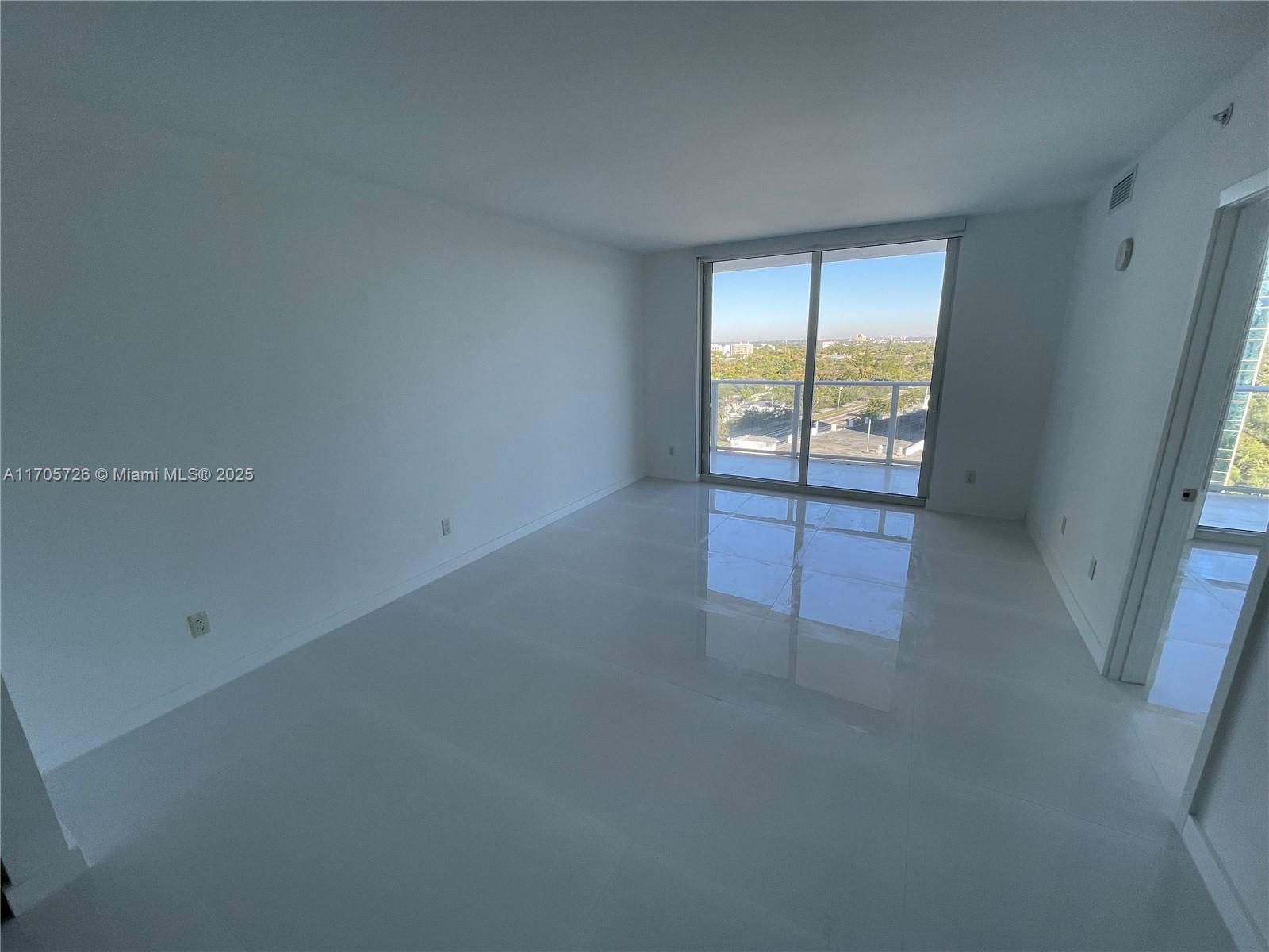 An empty room with white walls, glossy tile floors, and a sliding glass door to a balcony — 4250 Biscayne Blvd # 1104, Miami FL 33137, MIAMI, FL