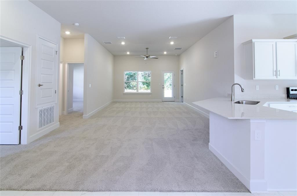 An open-concept living area features gray carpeting, white walls, a ceiling fan, and a kitchen — 35 FARNELL LANE, PALM COAST, FL