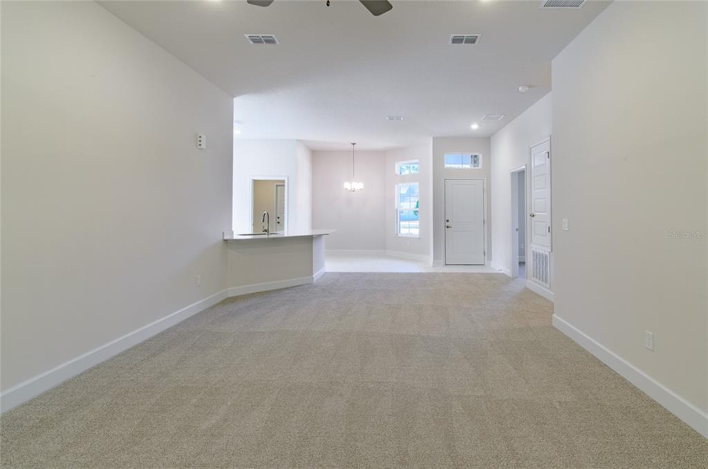 A spacious living area with beige carpeting leads to a kitchen and dining nook — 35 FARNELL LANE, PALM COAST, FL