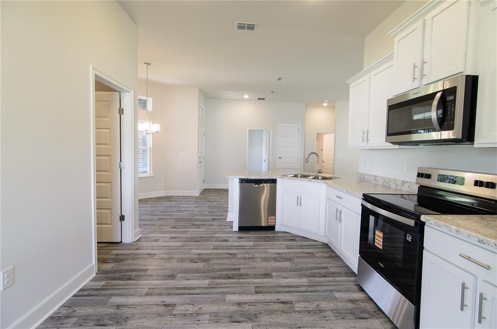 A kitchen with white cabinets, stainless steel appliances, and wood-look flooring opens to a dining area — 35 FARNELL LANE, PALM COAST, FL