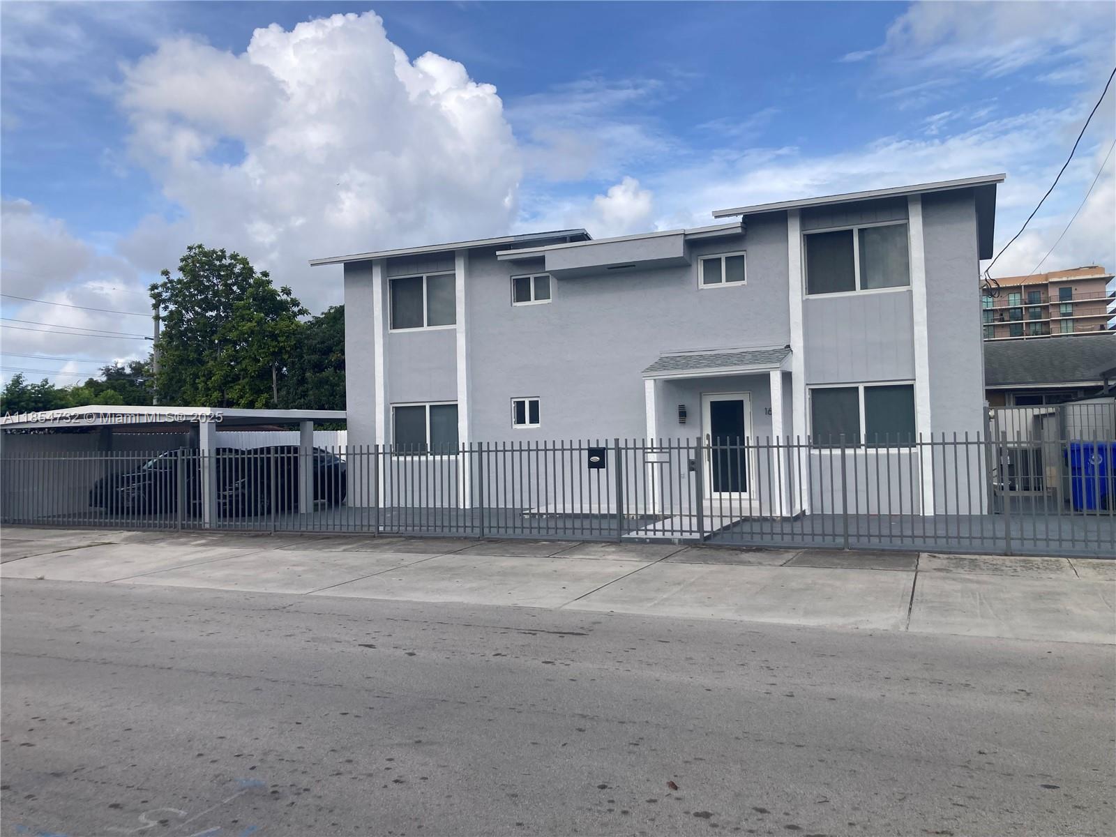 A two-story gray house with a metal fence and a covered carport under a cloudy sky — 1671 SW 29th Ave, Miami FL 33145, MIAMI, FL