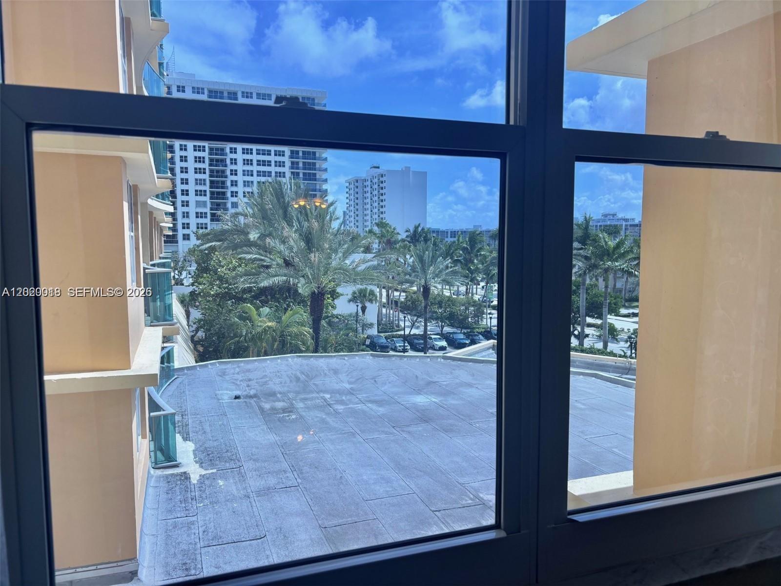 A view through a window shows a flat roof, palm trees, and nearby apartment buildings — 2501 S Ocean Dr # 433, Hollywood FL 33019, HOLLYWOOD, FL