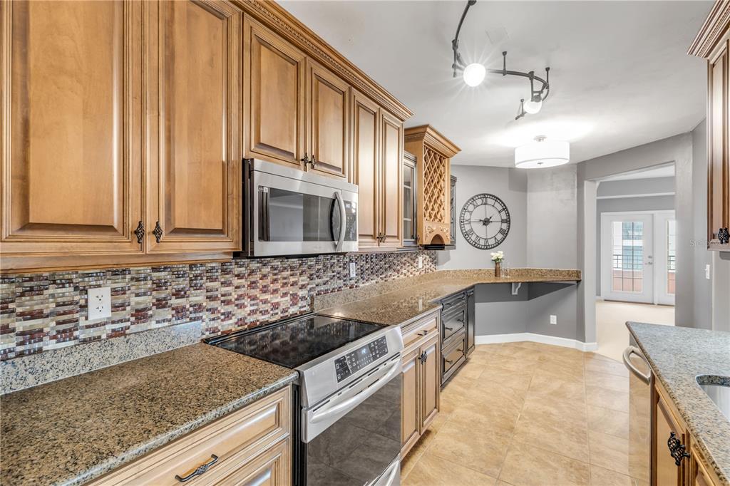 A kitchen features wood cabinets, granite countertops, a glass tile backsplash, and stainless steel appliances — 424 LUNA BELLA LANE UNIT 231, NEW SMYRNA BEACH, FL