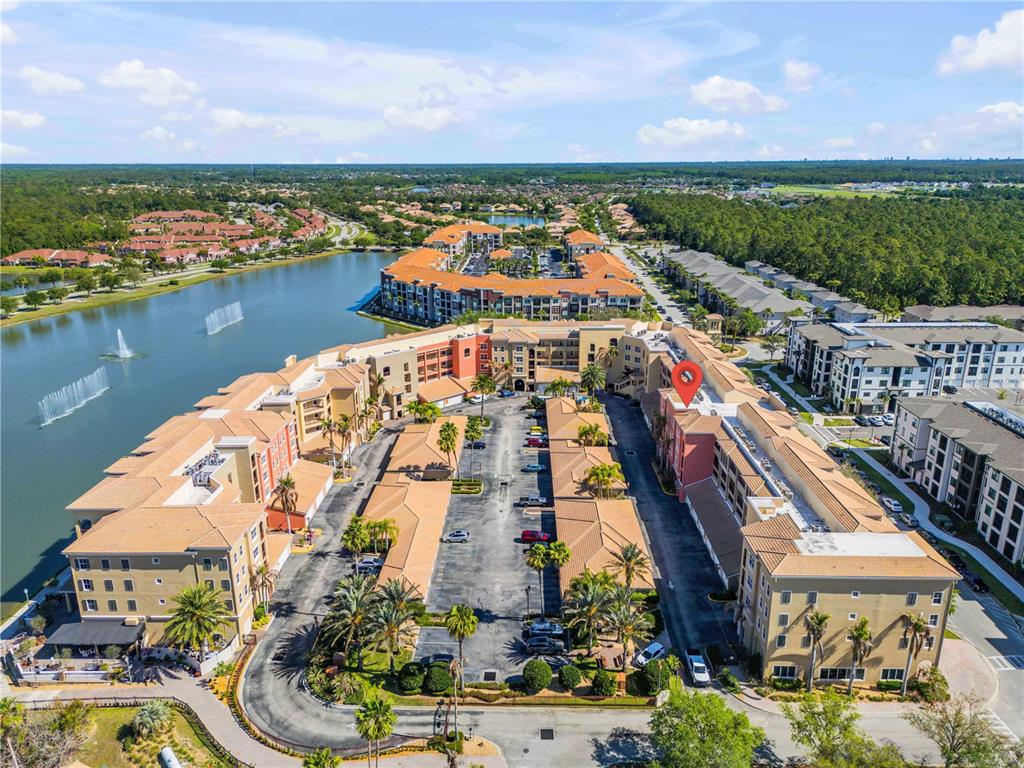 An aerial view shows a large apartment complex with a central parking lot and lake — 424 LUNA BELLA LANE UNIT 231, NEW SMYRNA BEACH, FL
