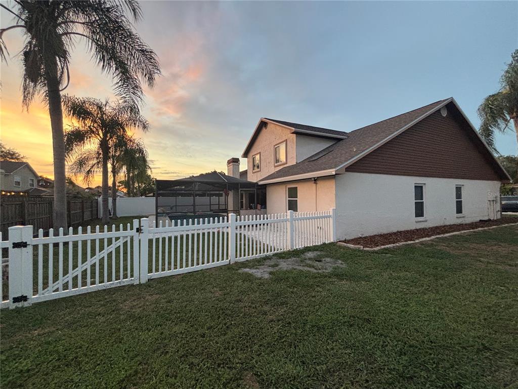 A white house with a screened-in pool area and a white picket fence at sunset — 1435 BUCKNER ROAD, VALRICO, FL