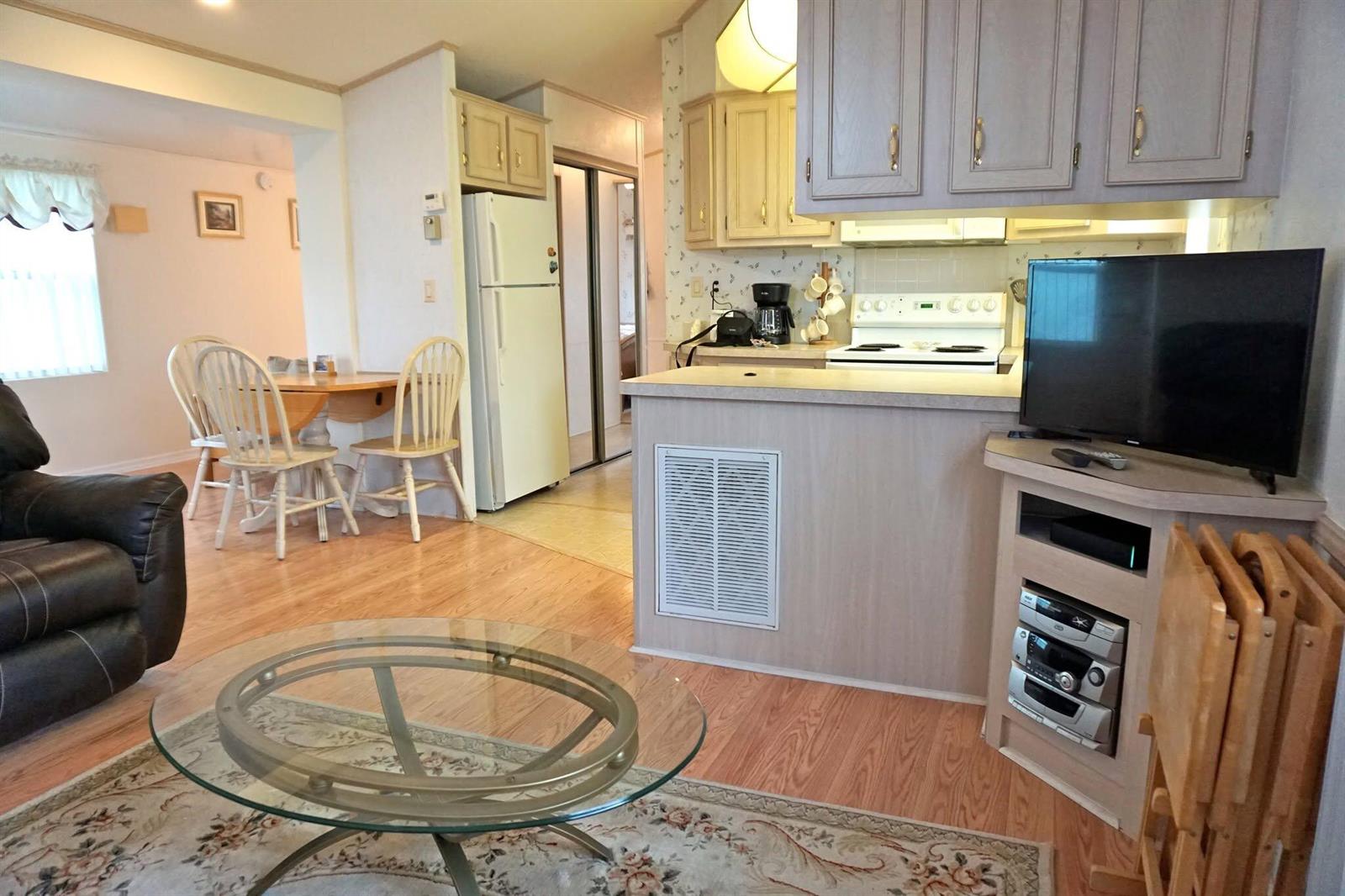 A living room and kitchen area featuring light wood cabinets, laminate flooring, and a television — 10725 S Ocean Drive # 265, Jensen Beach FL 34957, JENSEN BEACH, FL