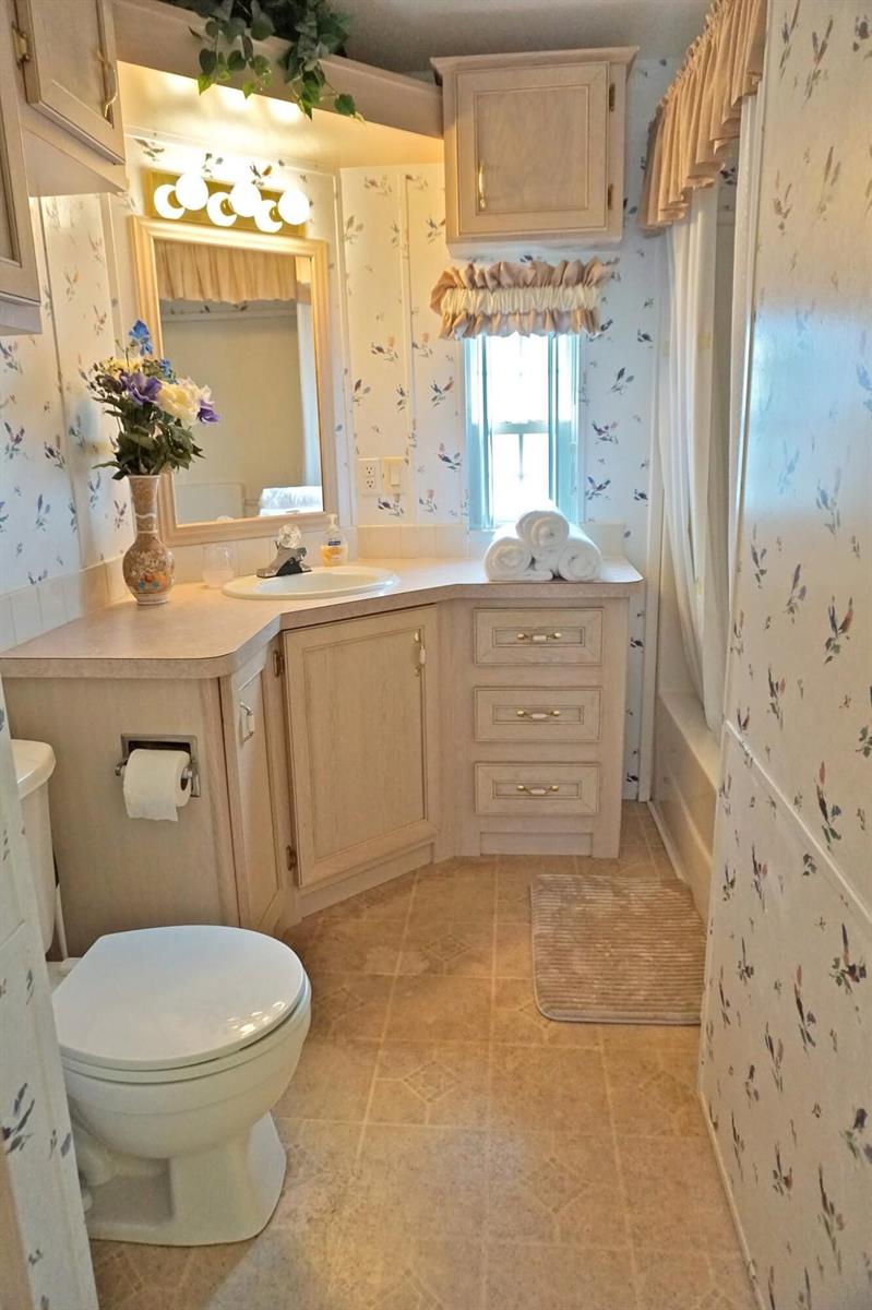 A bathroom features floral wallpaper, light wood cabinets, a corner vanity, and a shower-tub combination — 10725 S Ocean Drive # 265, Jensen Beach FL 34957, JENSEN BEACH, FL