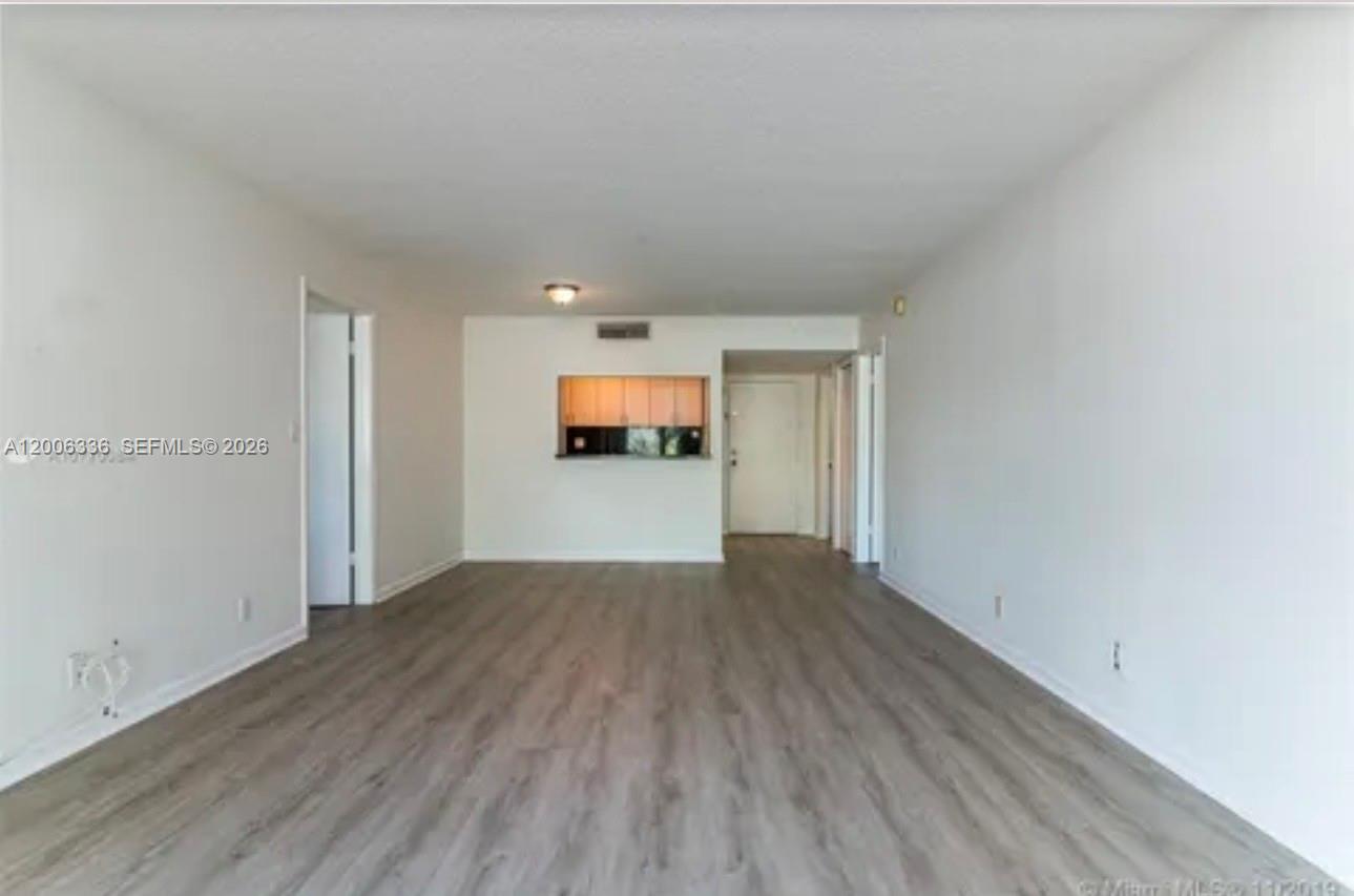 An empty living room features light wood-look flooring, white walls, and a kitchen pass-through window — 100 Lakeview Dr # 112, Weston FL 33326, WESTON, FL