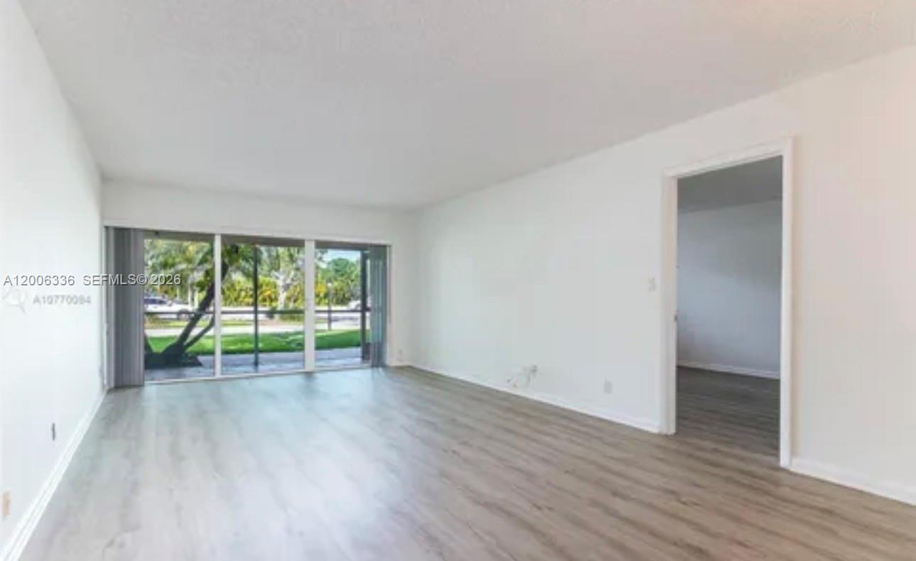An empty living room features light wood-look flooring, white walls, and large sliding glass doors — 100 Lakeview Dr # 112, Weston FL 33326, WESTON, FL