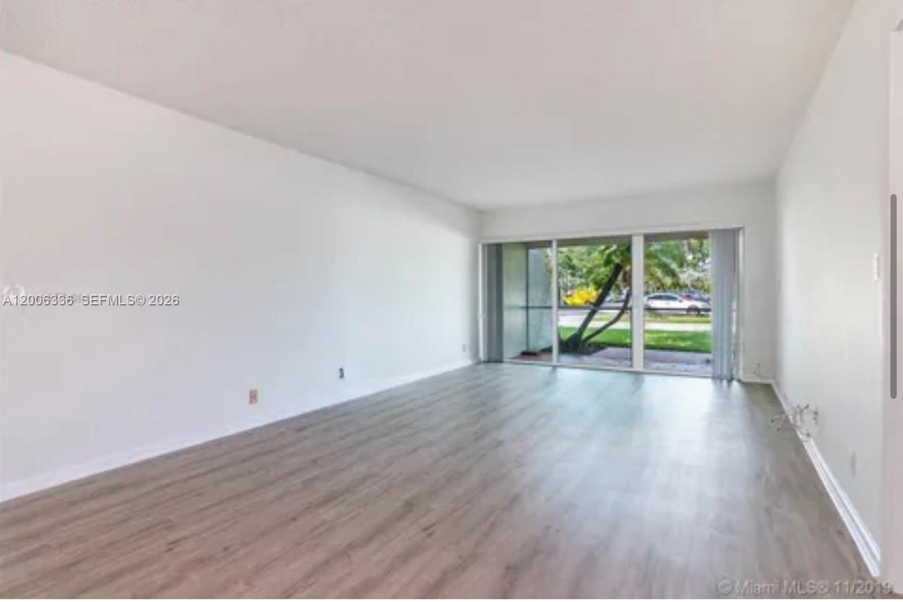An empty living room features light wood-look flooring, white walls, and a large sliding glass door — 100 Lakeview Dr # 112, Weston FL 33326, WESTON, FL