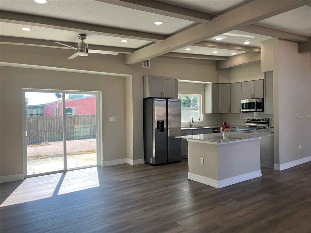 A kitchen with gray cabinets, stainless steel appliances, and an island opens to a living area — 725 SCENIC STREET, LEESBURG, FL