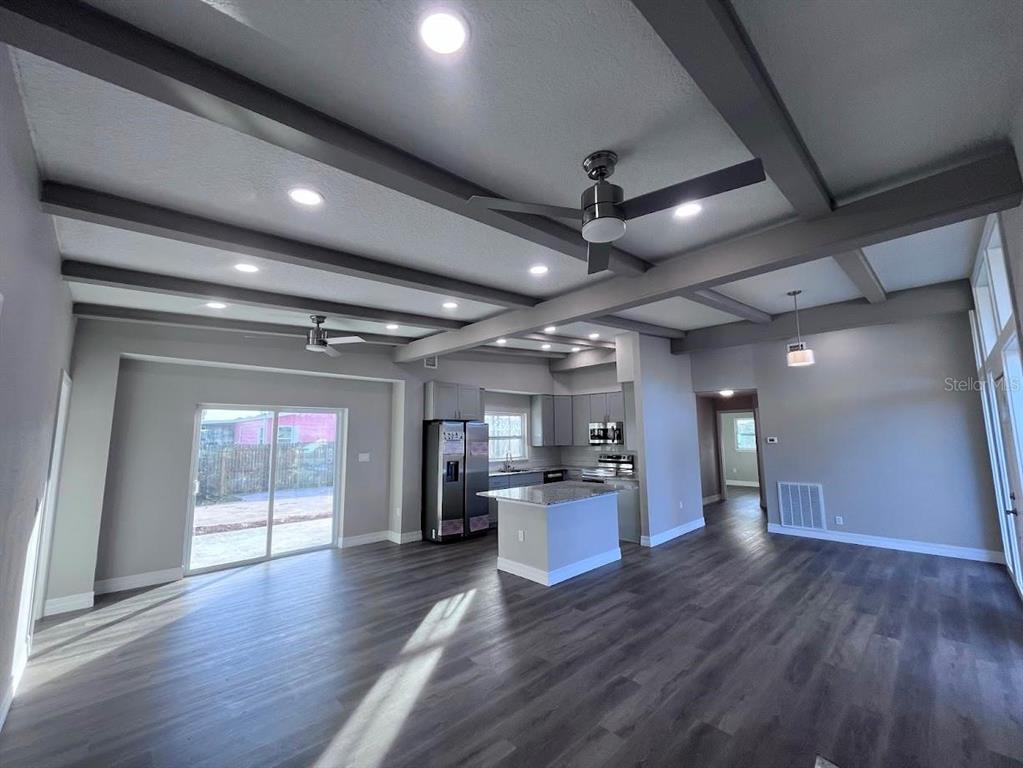 An open-concept kitchen and living area features gray wood-look flooring and exposed ceiling beams — 725 SCENIC STREET, LEESBURG, FL