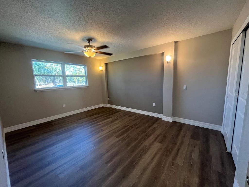 An empty bedroom features dark wood-look flooring, a ceiling fan, and a large window — 725 SCENIC STREET, LEESBURG, FL