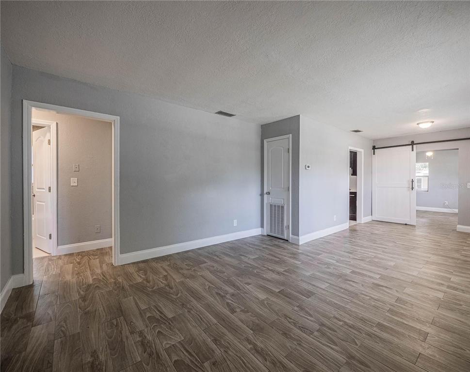 An interior view of a room with gray walls, wood-look flooring, and a white barn door — 2414 AVENUE A TERRACE NW, WINTER HAVEN, FL