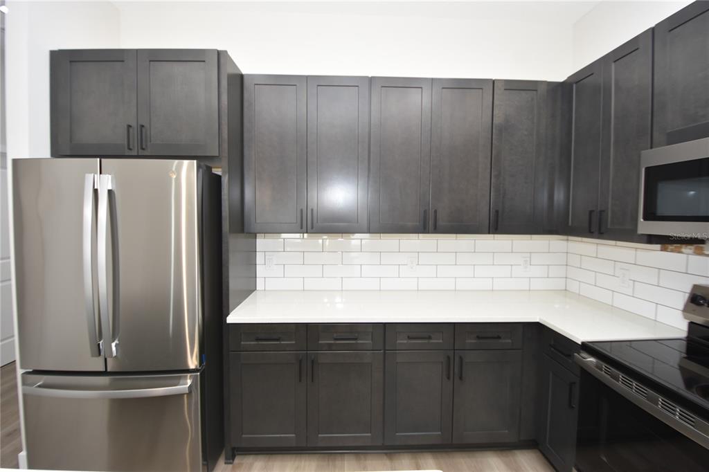 A kitchen features dark gray cabinets, white countertops, a subway tile backsplash, and stainless steel appliances — 5 SETON COURT UNIT B, PALM COAST, FL