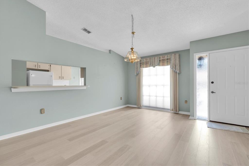 An empty dining room features light wood flooring, pale green walls, and a pass-through window — 2023 NASH DRIVE, CLEARWATER, FL