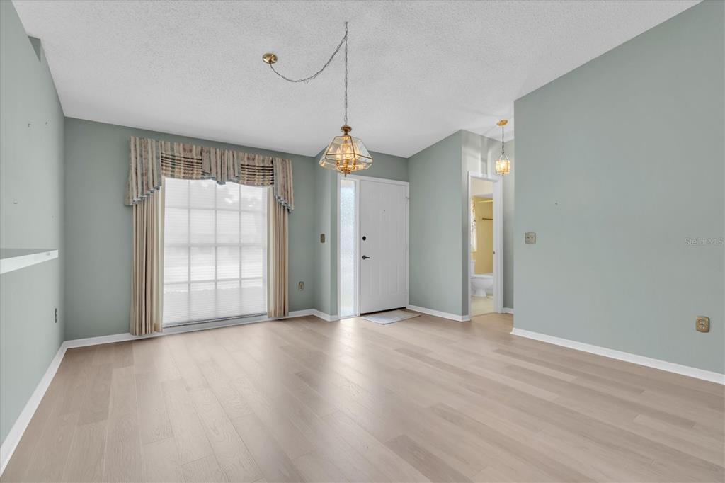An empty room with light wood flooring, sage green walls, a window, and two hanging lights — 2023 NASH DRIVE, CLEARWATER, FL