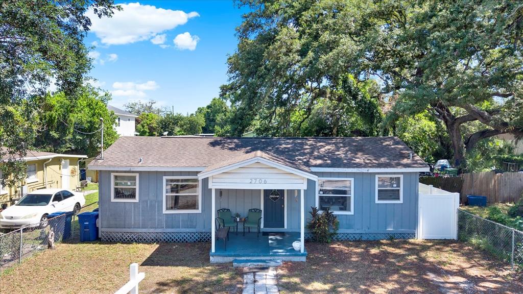 A single-story blue house with a front porch and a white fence sits under trees — 2706 E 22ND AVENUE, TAMPA, FL