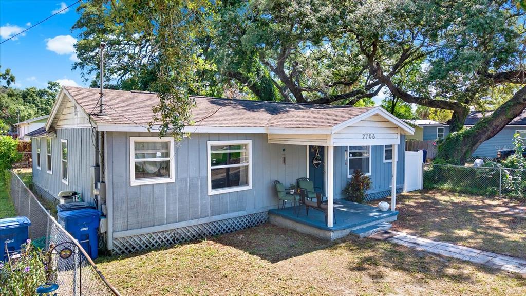 A single-story house with gray siding, a covered front porch, and large oak trees — 2706 E 22ND AVENUE, TAMPA, FL