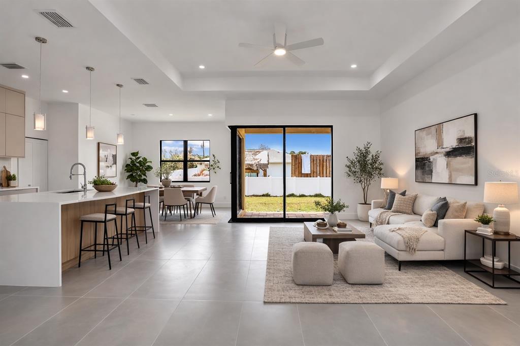 An open-concept living room and kitchen feature white cabinetry, tile flooring, and sliding glass doors — 6191 KAMBACH STREET, PORT CHARLOTTE, FL
