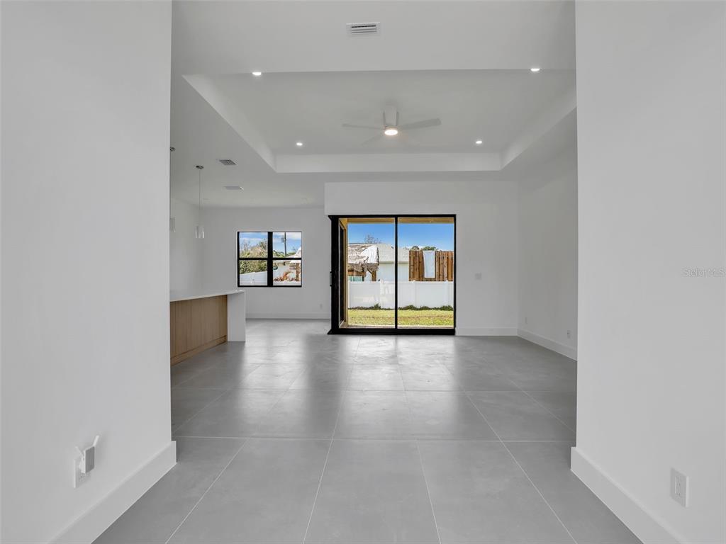 An open-concept living area features a tray ceiling, light gray tile flooring, and sliding glass doors — 6191 KAMBACH STREET, PORT CHARLOTTE, FL