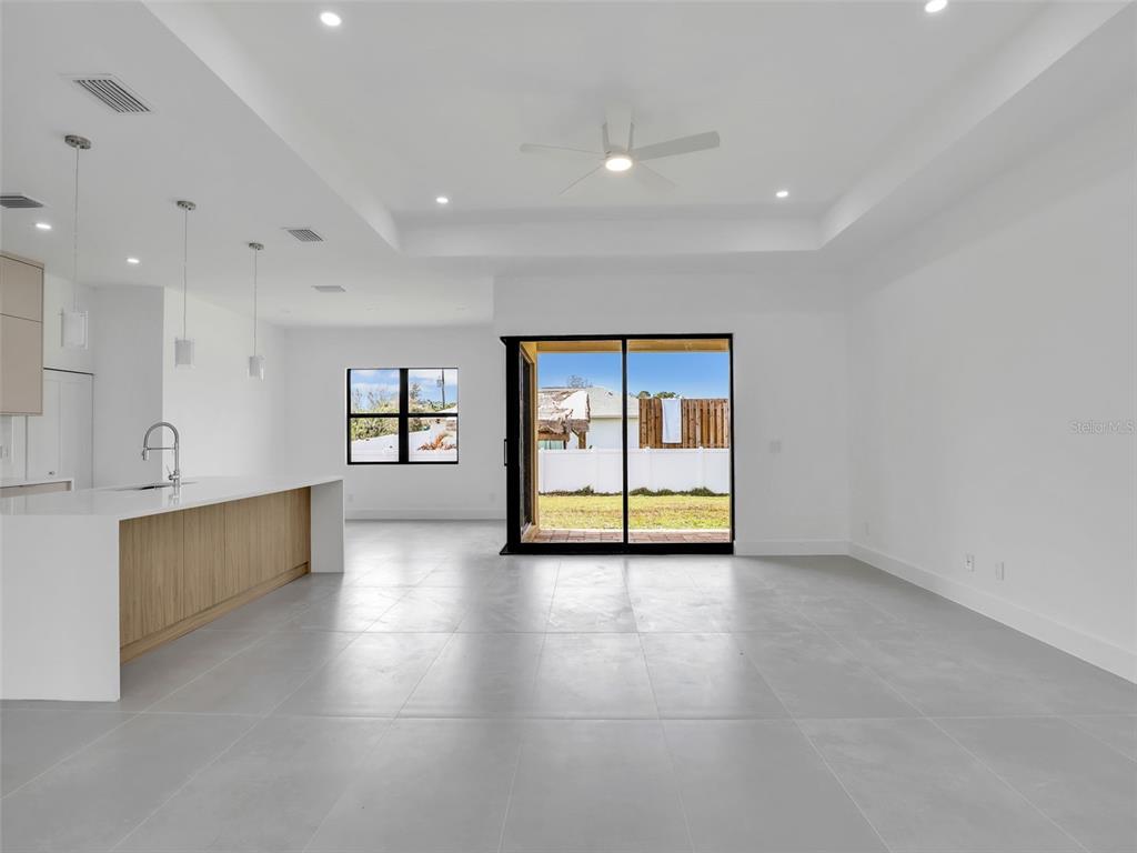 A modern open-concept kitchen and living area with white walls, gray tile floors, and sliding doors — 6191 KAMBACH STREET, PORT CHARLOTTE, FL