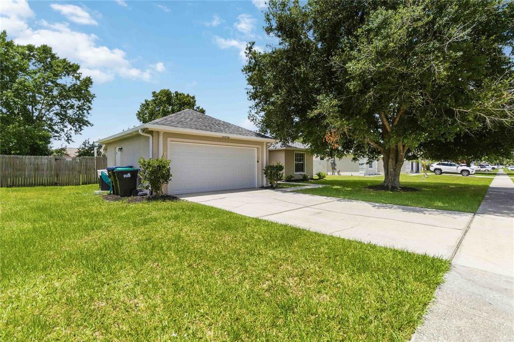 A single-story house exterior with a two-car garage, concrete driveway, and a large shade tree — 20446 MACON PARKWAY, ORLANDO, FL