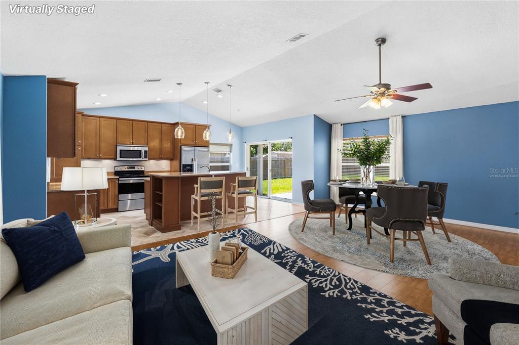 This virtually staged open-concept living, dining, and kitchen area features blue walls and wood cabinetry — 20446 MACON PARKWAY, ORLANDO, FL
