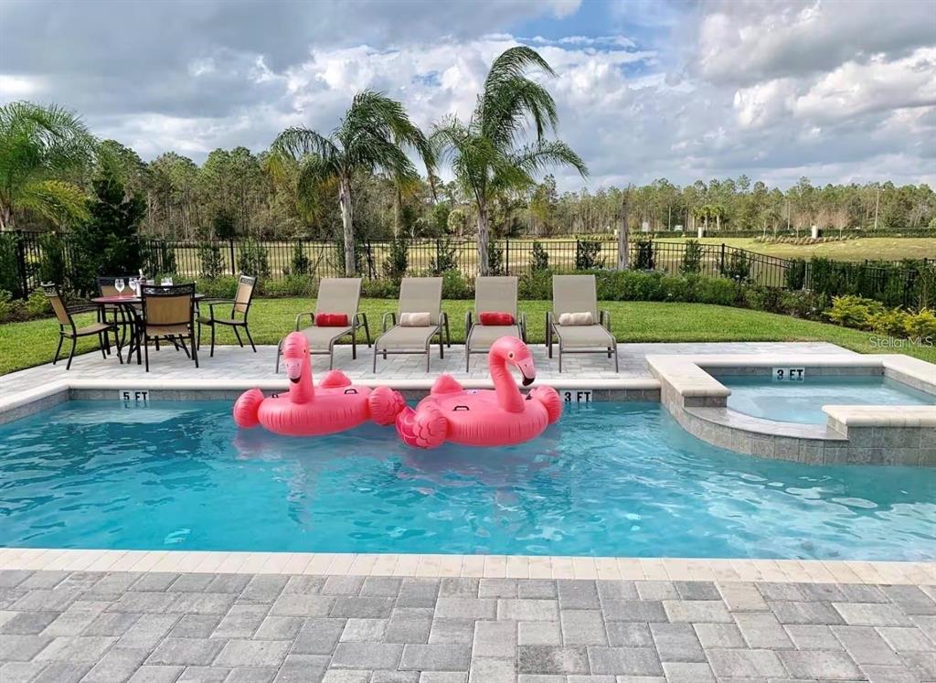 A swimming pool with two pink flamingo floats sits in front of a patio area — 7738 FAIRFAX DRIVE, KISSIMMEE, FL