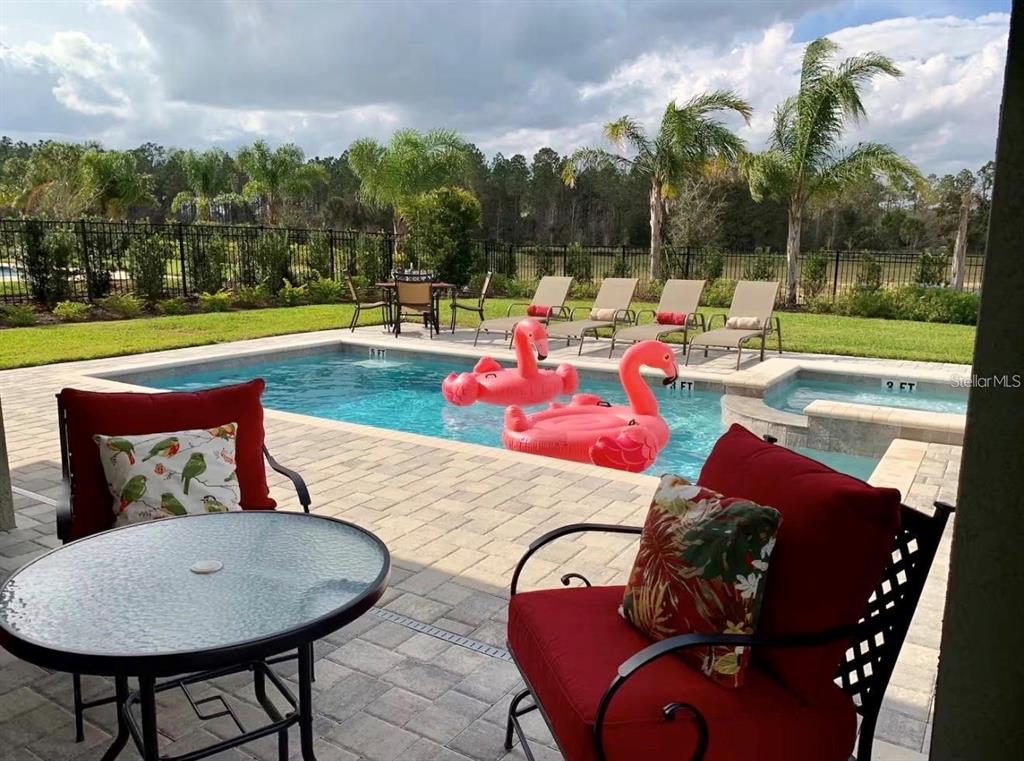 A patio with red chairs and a table overlooks a swimming pool with flamingo floats — 7738 FAIRFAX DRIVE, KISSIMMEE, FL