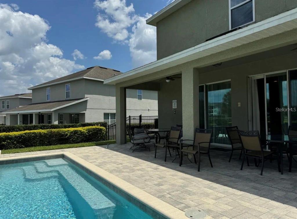 A covered patio with outdoor furniture overlooks a swimming pool and neighboring houses — 7738 FAIRFAX DRIVE, KISSIMMEE, FL