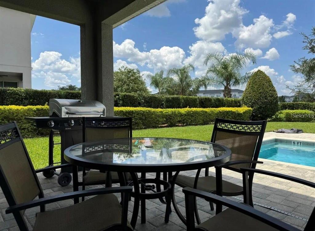 A covered patio features a glass-top dining set, a grill, and a view of a pool — 7738 FAIRFAX DRIVE, KISSIMMEE, FL