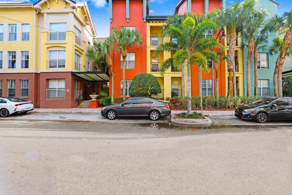 A street-level view of colorful multi-story apartment buildings with palm trees and parked cars — 2440 W HORATIO STREET UNIT 1012, TAMPA, FL