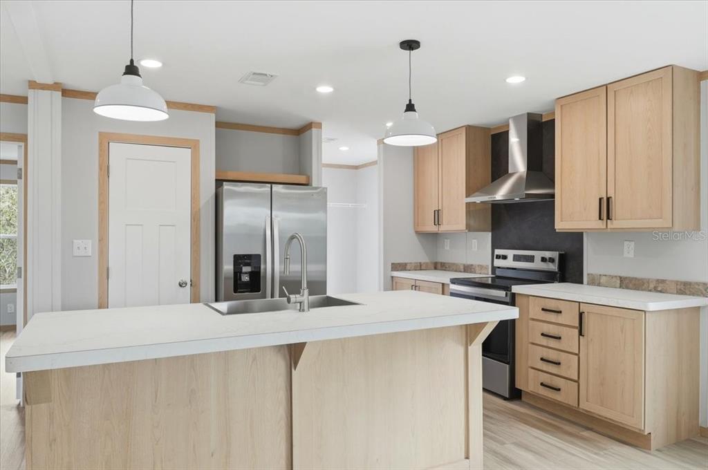 A kitchen features light wood cabinets, a white island, stainless steel appliances, and pendant lighting — 449 STONE STREET, WILDWOOD, FL